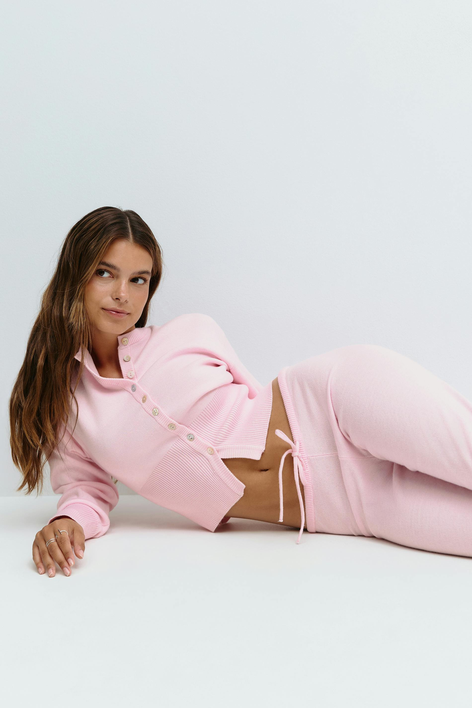 Pink knitted cardigan and trousers set, model reclining