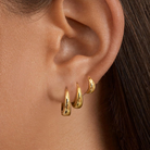 Close-up of gold huggie hoop earrings worn on model's ear
