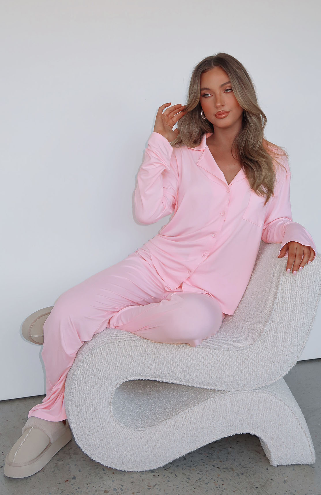 Pink long-sleeve pyjama set, model seated on boucle chair