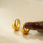 Pair of gold huggie hoop earrings on sand with driftwood
