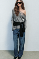 Grey asymmetric lace top styled with jeans and a knotted sweater, front view