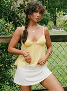 Yellow lace cami top with white skirt, model outdoors by fence